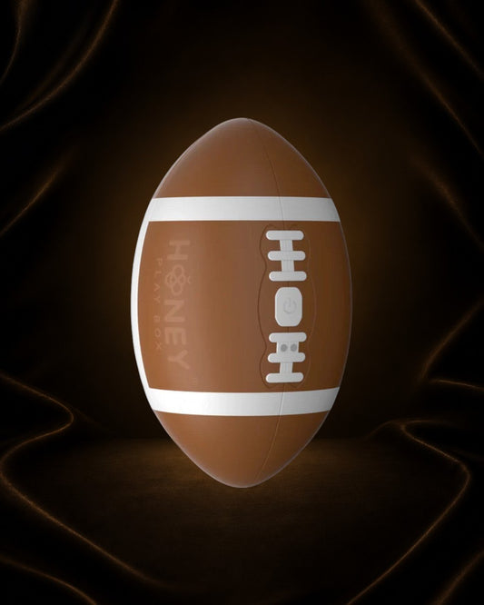 Éxtasis Boutique Masturbador Touchdown, diseño de balón de fútbol americano marrón con rayas blancas y detalles de costura, con dos motores para estimulación vibratoria.